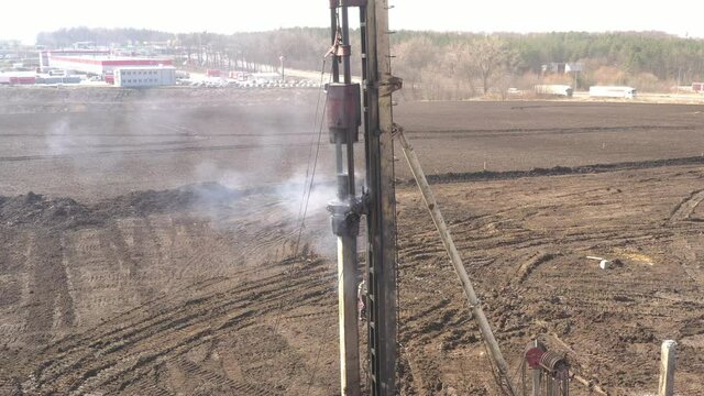 Excavation at a construction site, diesel pile driving machine with rumble and smoke drives piles deep into the ground to ensure the strength of the foundation of the future structure