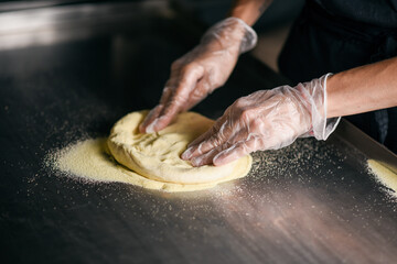 blurred image of yeast dough on an iron kitchen table kneading hands of a cook in gloves and a black apron
