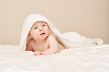 Fototapeta na wymiar Cute small boy lying at bed. Childhood bath concept. Light background. Little child. Serious emotion. Copyspace. Stay home. Towel mockup