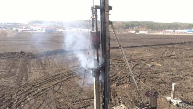 Excavation at a construction site, diesel pile driving machine with rumble and smoke drives piles deep into the ground to ensure the strength of the foundation of the future structure