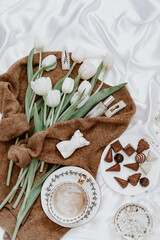 Bouquet of white tulips with sweater for womens day, coffee cup and chocolate, still life concept of spring flowers. Blogger background