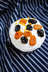 An Easter cake decorated with dried apricots and prunes stands on a striped blue apron. Easter religious holiday concept.