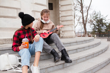 Group of kids resting outdoor in the street, playing in ukulele, sing song eat and drink juice