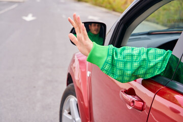 Rear view of a driver's arm waving to someone from a moving car.