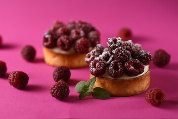 French Pastry - A tartlet with a fruity filling and a crispy baked base. french dessert on a pink background with fresh raspberries and a sprig of mint