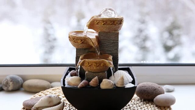 Portable indoor fountain for good Feng Shui in Your Home concept. Portable indoor small tabletop fountain on window sill, decorated with seashells and stones. Spiritual mind and soul balance concept.