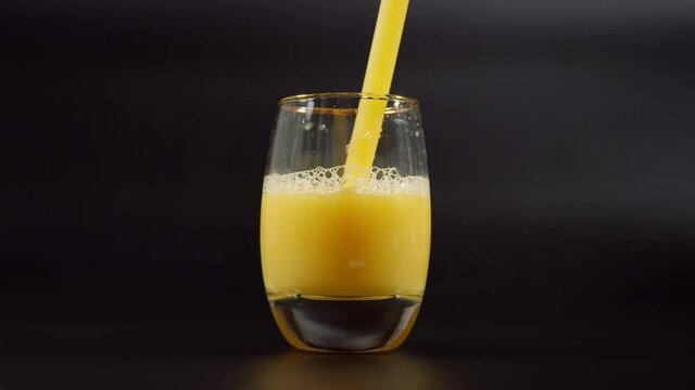 Drinking orange juice from straw. Close up on luxury glass filled with orange juice standing on dark background.
