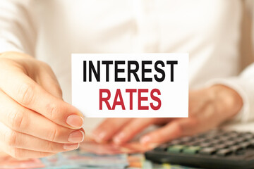 a woman in a white shirt holds a piece of paper with the text: interest rates, business concept.