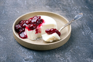 Modern style traditional blancmange almond pudding with sour cherry coulis served as close-up in a Nordic design plate on gray background