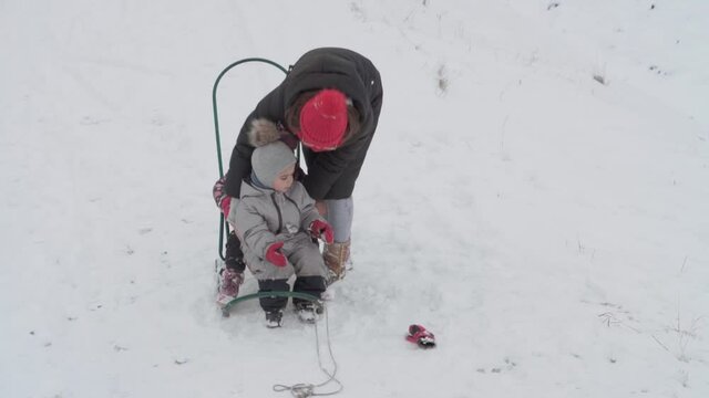vacation, game, family concept - slo-mo authentic three happy preschool toddler kids siblings with young wonan mom sledding and play with snow. snowfall in cold season weather in winter yard outdoors