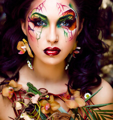 beauty woman with face art and jewelry from flowers orchids close up, creative makeup floral pattern background