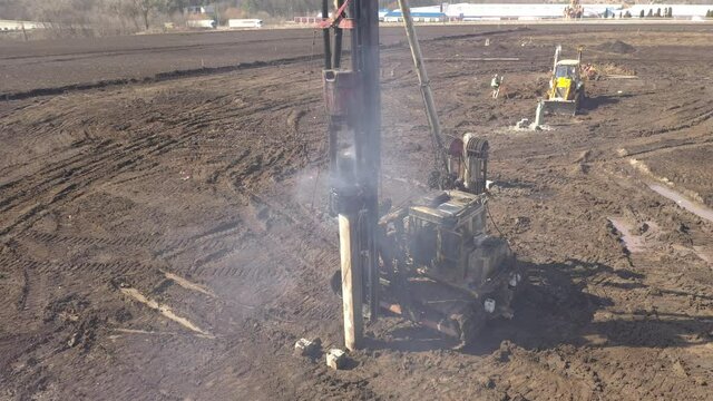 Excavation at a construction site, diesel pile driving machine with rumble and smoke drives piles deep into the ground to ensure the strength of the foundation of the future structure