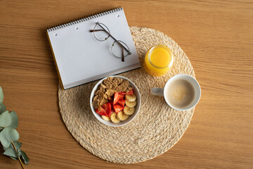 Mesa con mantel individual de yute con zumo café bol de frutas gafas y libreta