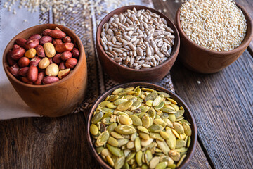 Peeled pumpkin, sunflower, nut, and sesame seeds in a wooden bowl on a wooden table. Bakery ingredients. Products for tasty and healthy food.