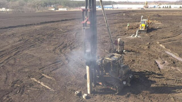 Excavation at a construction site, diesel pile driving machine with rumble and smoke drives piles deep into the ground to ensure the strength of the foundation of the future structure