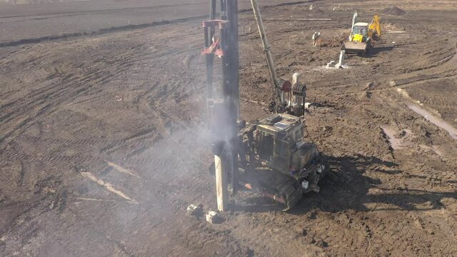 Excavation at a construction site, diesel pile driving machine with rumble and smoke drives piles deep into the ground to ensure the strength of the foundation of the future structure