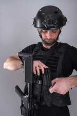 Close up of male equipped for airsoft adding an extra magazine to his vest while looking down.