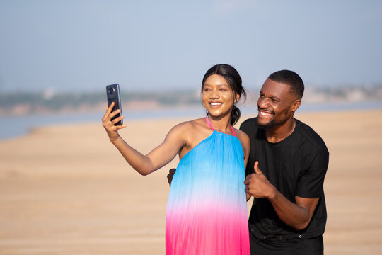 young african man and woman taking a selfie together on a beach on vacation