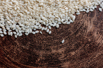 Organic natural white sesame seeds on dark brown clay dishes background. Close up macro shot sesam, top view.
