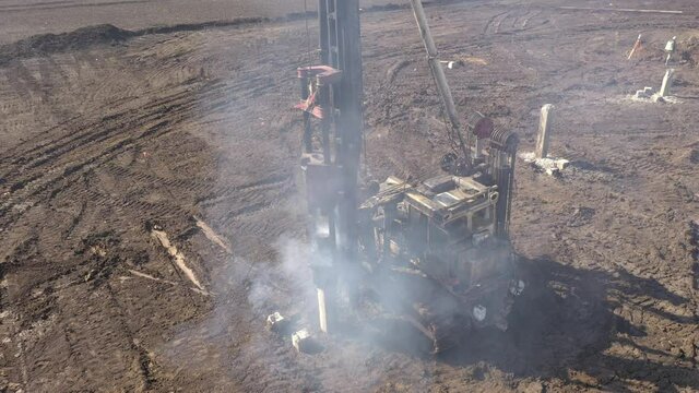 Excavation at a construction site, diesel pile driving machine with rumble and smoke drives piles deep into the ground to ensure the strength of the foundation of the future structure