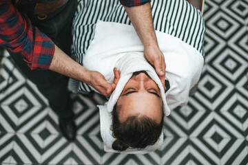 The barber trims the beard of the customer in his barber shop. Trendy and stylish beard styling and...