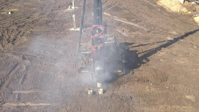 Excavation at a construction site, diesel pile driving machine with rumble and smoke drives piles deep into the ground to ensure the strength of the foundation of the future structure