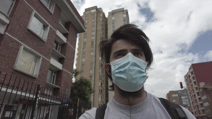 Young caucasian man with face mask with urban buildings and cityscape of Bogota, Colombia behind. Slow motion footage. Scene of new normal after quarantine of COVID-19 or coronavirus pandemic. - Powered by Adobe