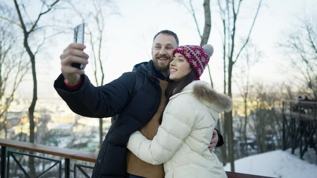 Happy cheerful romantic couple at sunny winter day. They do a selfie on a smartphone. Filmed on cinema camera, 10 bit color space.