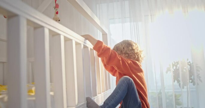Boy climbing on bed at home. Tracking shot of boy with curly hair climbing on bunk bed in light nursery at home