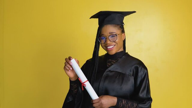African american female has got master's degree after graduating the university. Happy female student with diploma on yellow background