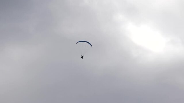 Paraglider, acropilot. Aerobatics. Acreage. A helicopter. Blue wing. Gray sky.