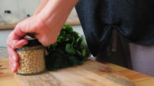 A woman in a bright kitchen opens a jar of pine nuts. Preparing breakfast close-up in slow motion.