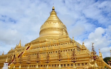 Fototapeta premium Shwezigon Pagoda, the golden temple in Bagan shines brilliantly under sunlight and in background of cloudy sky