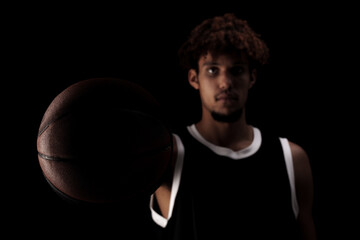 Professional basketball player holding a ball against black background. Serious concentrated african american man in sports uniform