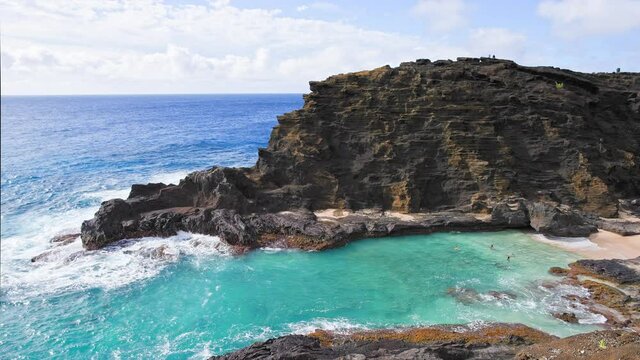 People swim in the turquoise waters of the Tropical Beach. Halona Beach Cove. Blue Waves of the Pacific Ocean Beats Oahu Island Volcanic Cliffs. Clear sunny day. DCI 4k