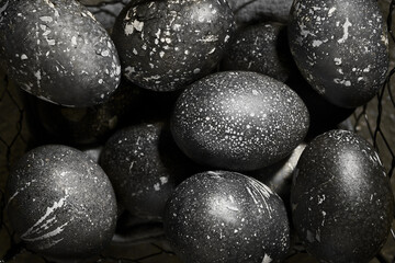 Black painted eggs for Easter in a basket, like a stone, on a gray vintage background
