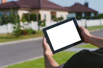 A tablet in the hands of a man, against the backdrop of a house.