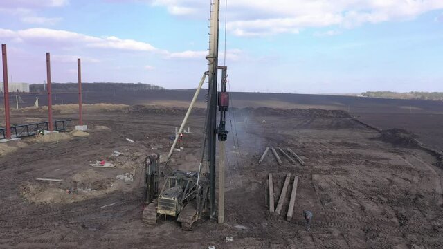 Excavation at a construction site, diesel pile driving machine with rumble and smoke drives piles deep into the ground to ensure the strength of the foundation of the future structure