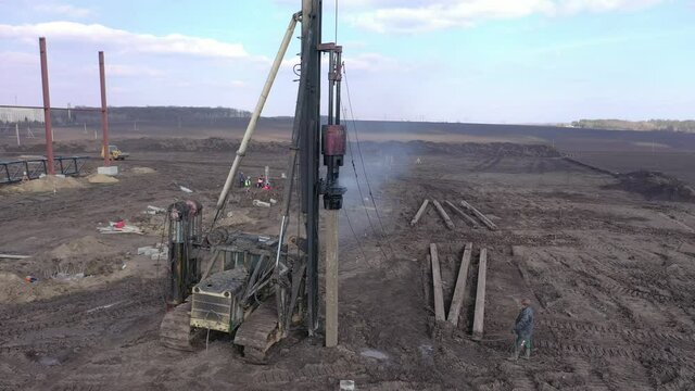 Excavation at a construction site, diesel pile driving machine with rumble and smoke drives piles deep into the ground to ensure the strength of the foundation of the future structure