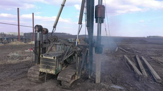 Excavation at a construction site, diesel pile driving machine with rumble and smoke drives piles deep into the ground to ensure the strength of the foundation of the future structure