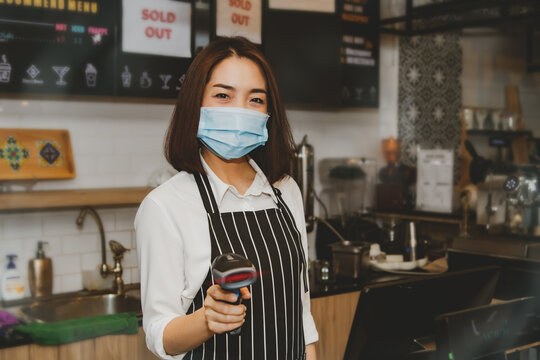 Trades and technology concept : Asian business women coffee shops use modern barcode scanners for convenience and speed for customer service during the Covid-19 epidemic.
