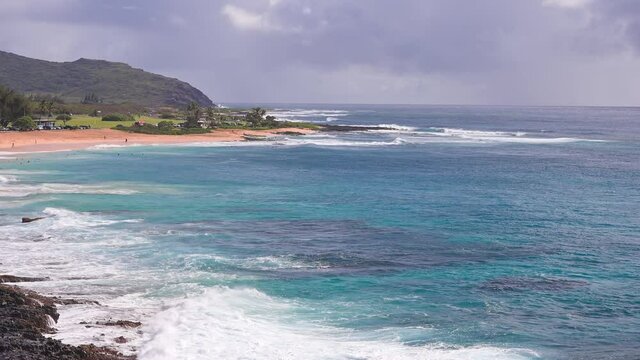 People swim in the turquoise waters of the Tropical Beach. Sandy Beach. Blue Waves of the Pacific Ocean Beats Oahu Island Volcanic Cliffs. Ke One Kula Lookout. Clear sunny day. DCI 4k