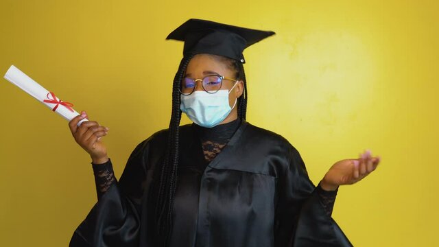 The african american female graduate student in a protective mask and with a diploma in hand expresses the gesture of the need to comply with quarantine security measures. Education concept