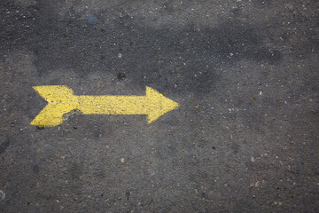 Yellow arrow painted on concrete sidewalk pointing right