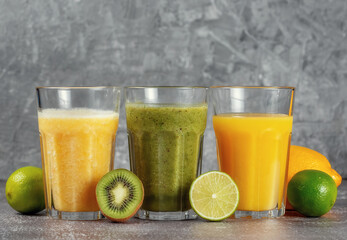 Three glasses in a row with orange juice and banana orange kiwi smoothie