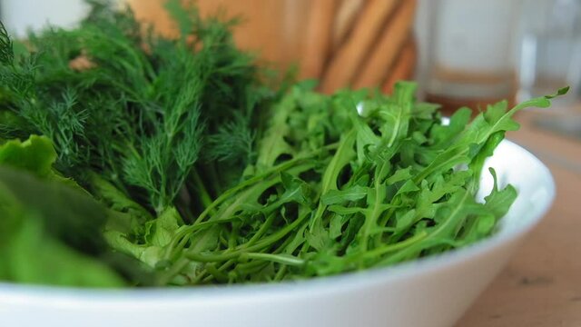 The chef chooses fresh salad and herbs for breakfast, lunch, dinner. Female hands choose salad, dill, spinach, rucola in a light kitchen in a white dish. Slow-mo
