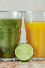 Two tall glass with kiwi and spinach smoothies surrounded by fruits on a wooden