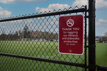 Smoke-free zone sign on chain link fence with university green grass playing field in background
