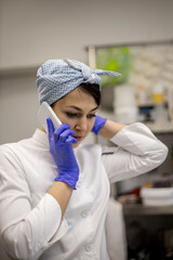 Female confectioner talking use smartphone working catering cuisine with stack of rubber mold tray