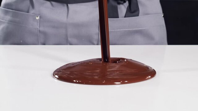 Pastry chef in grey uniform tempering melted chocolate on a white stone table using a scraper and pyrometer. Confectioner chocolate tempering